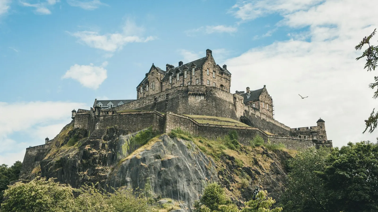 Edinburgh Castle på den bratte vulkanklippen Castle Rock under blå himmel med skyer