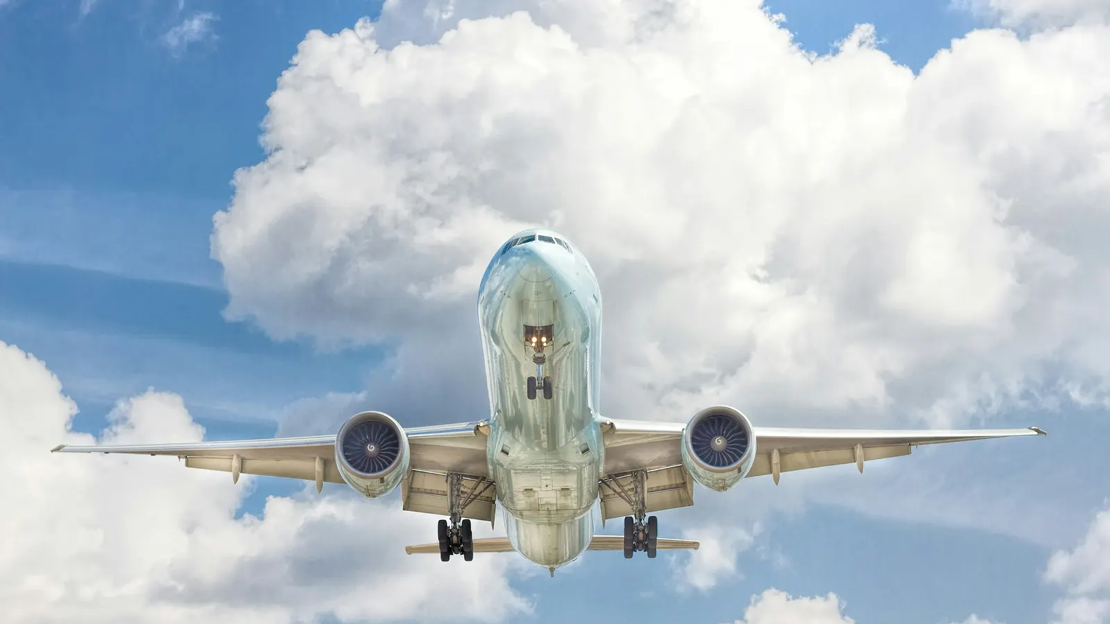 Passasjerfly med utfelt understell på vei inn for landing under blå himmel med hvite skyer