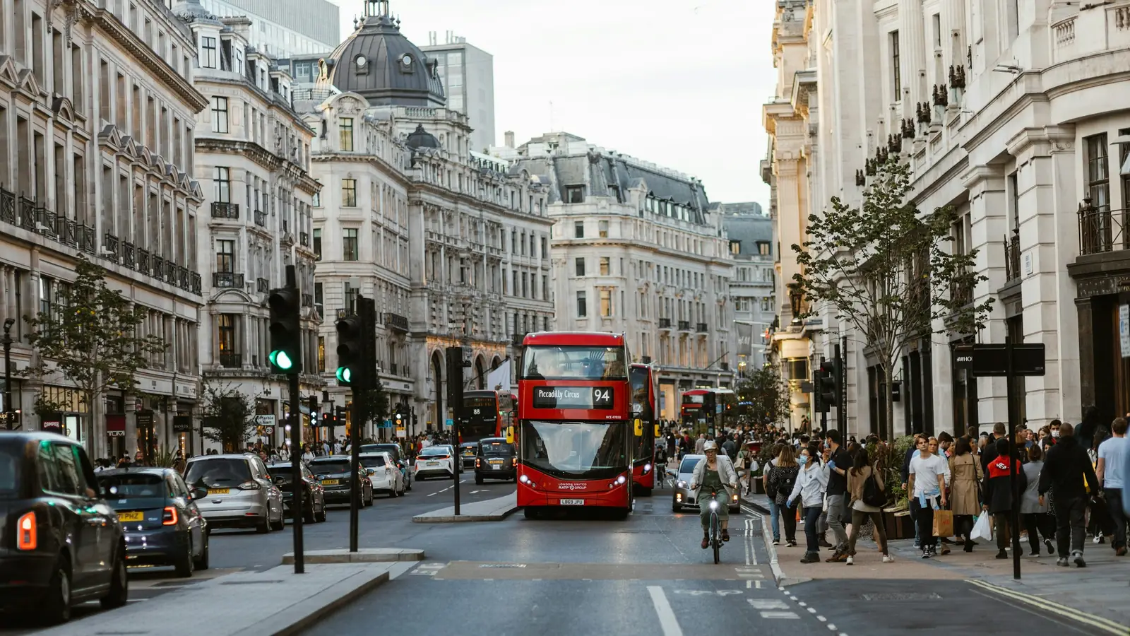 Travel handlegate i London med rød dobbeltdekkerbuss, taxier og elegante bygninger på begge sider