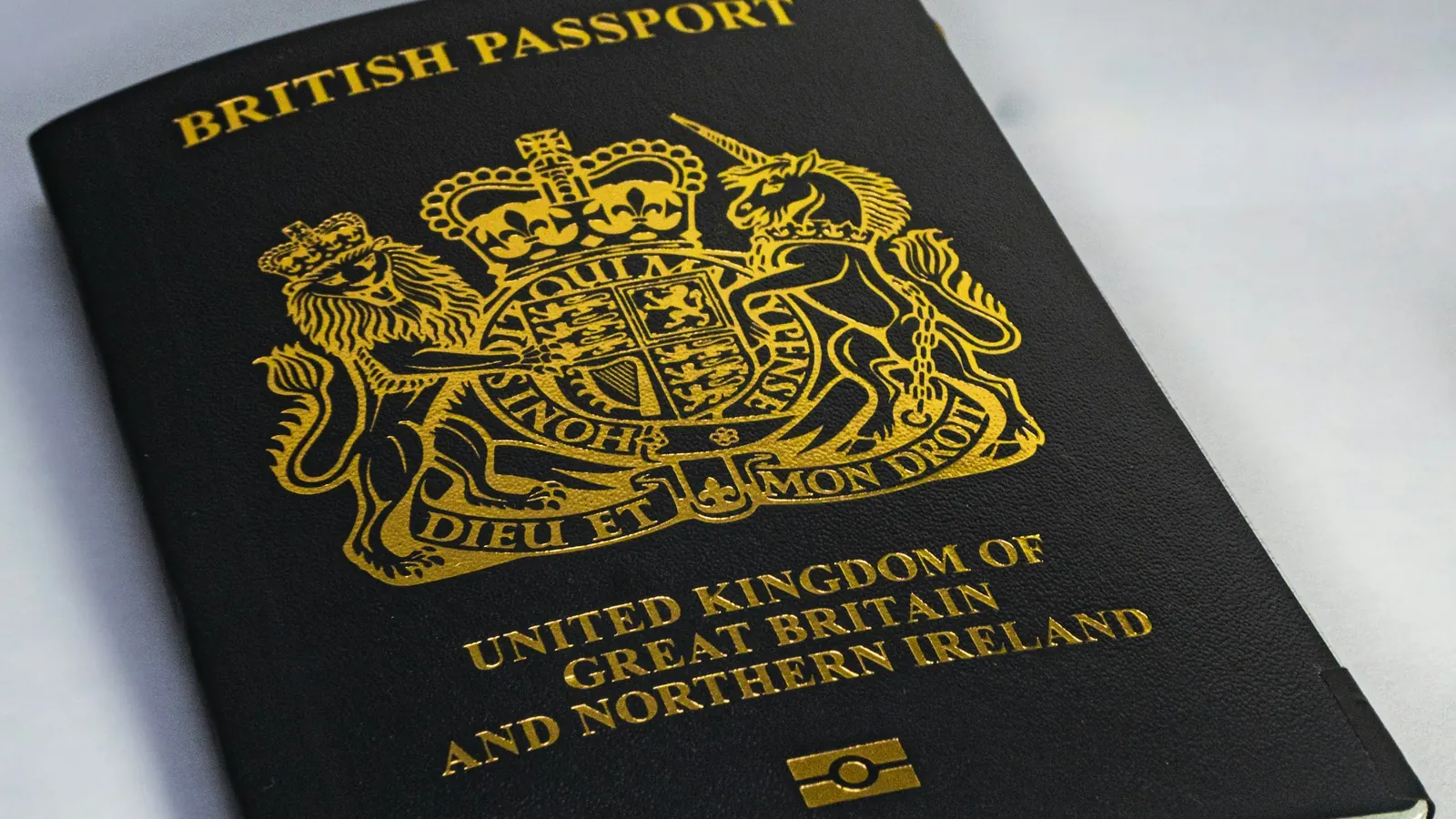Nærbilde av et mørkeblått britisk pass med gullfarget riksvåpen på et hvitt bord